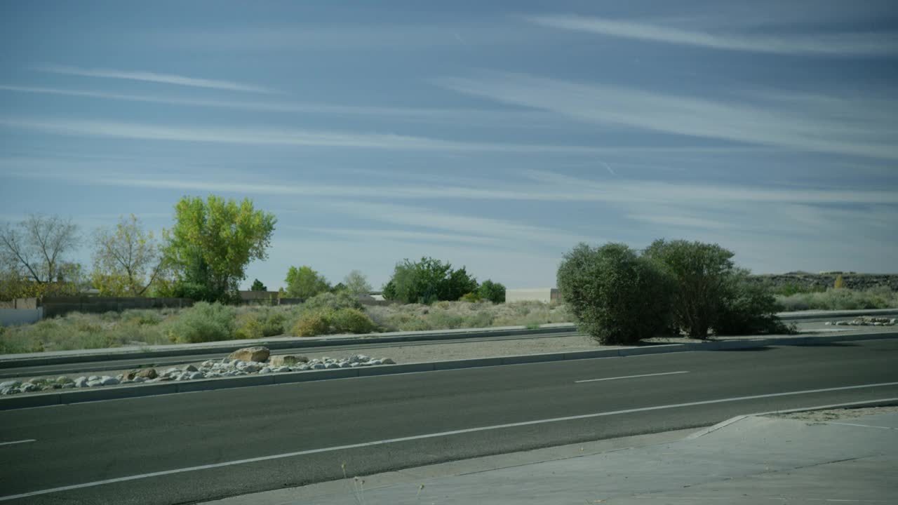 当汽车从右到左行驶时，道路的中等角度。中间有灌木和岩石可见。在bg中可见的树。农村地区。蓝色的天空。视频素材