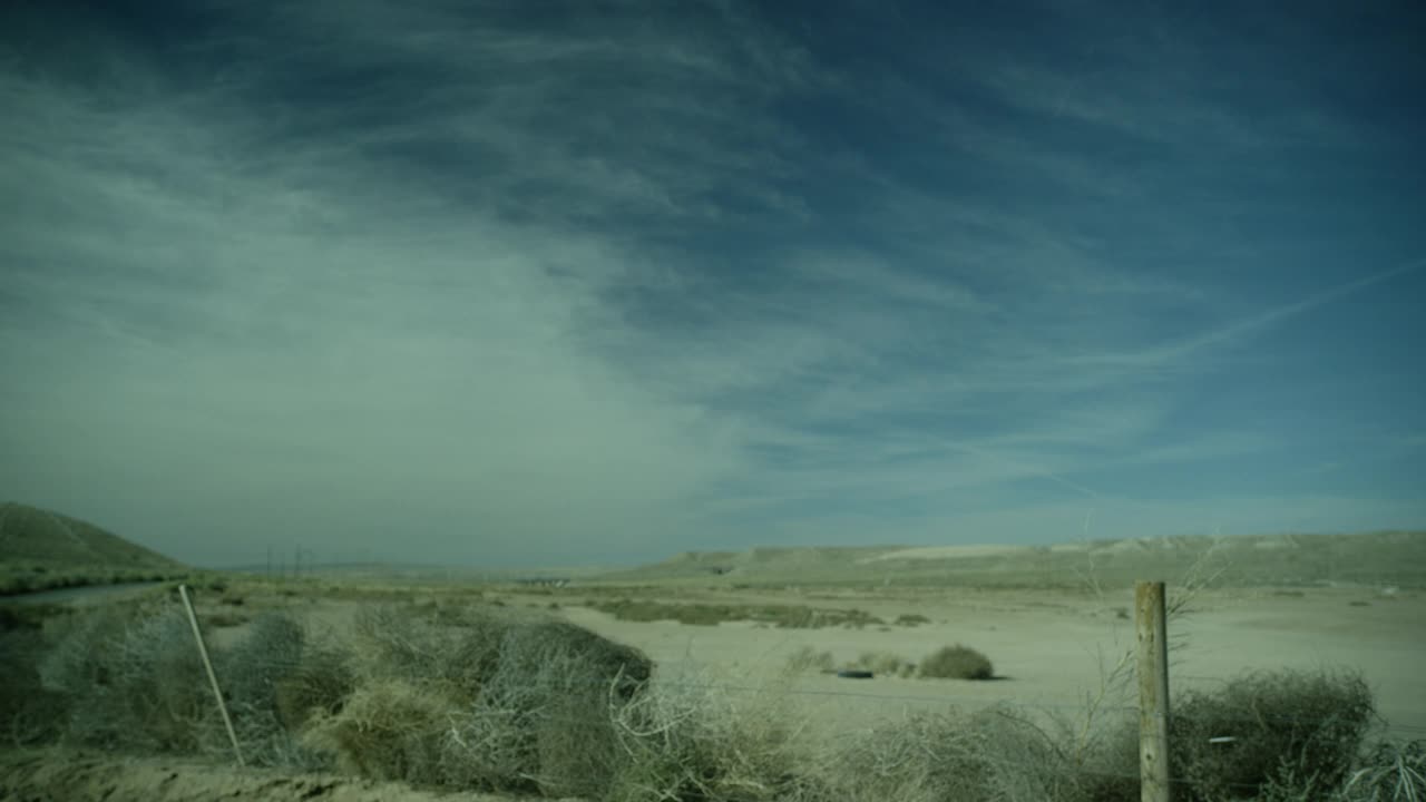 乡村公路或沙漠公路旁干燥沙漠地区的广角。可能是农田。在fg中可见带刺铁丝网围栏和灌木。蓝天白云。视频素材