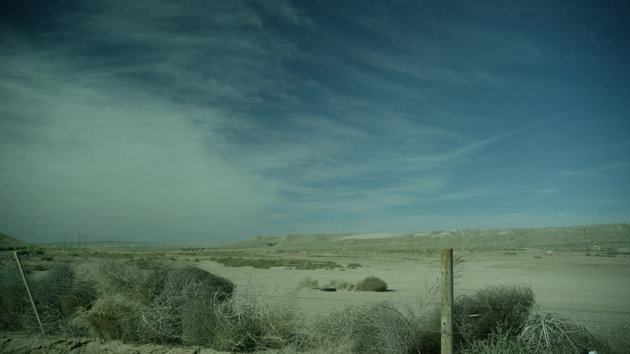 乡村公路或沙漠公路旁干燥沙漠地区的广角。可能是农田。在fg中可见带刺铁丝网围栏和灌木。蓝天白云。视频素材