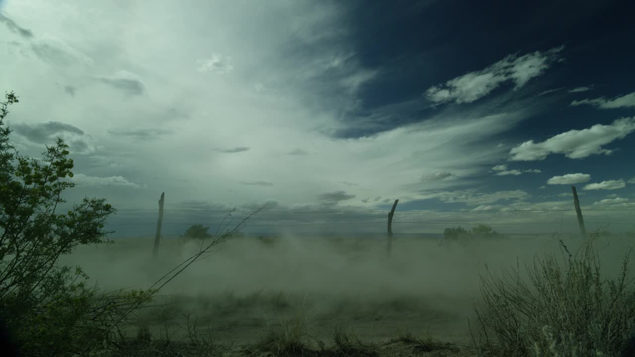 在沙漠，农村地区，农田或乡村的中等角度的土路。可见铁丝网栅栏。扬起的灰尘可能是车里的。干枯的草、灌木、蓝天白云都清晰可见。视频素材