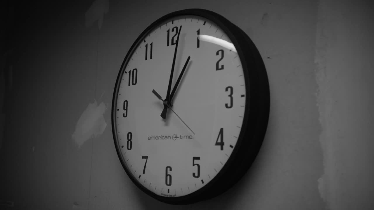 墙上时钟的闭合角度。时钟读取一点。可能是休息室。墙上的油漆未完成。黑白照片。视频素材