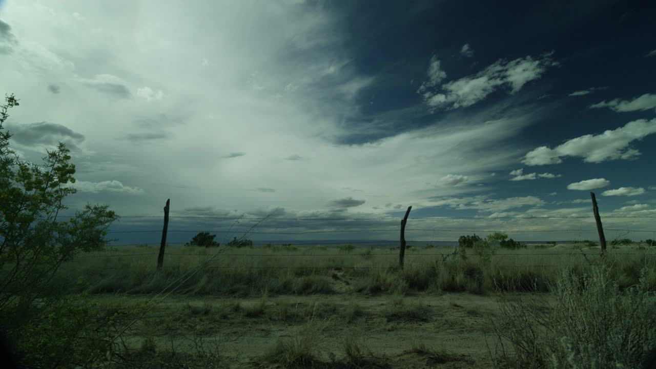 在沙漠，农村地区，农田或乡村的中等角度的土路。铁丝网栅栏可见…干枯的草、灌木、蓝天白云都清晰可见。视频素材