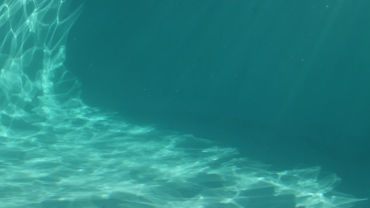 从右到左在水下的阳光照射在游泳池的墙壁上。视频素材