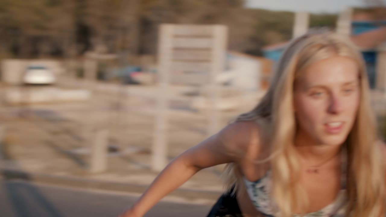 年轻的女人在夏天的阳光下围着相机滑滑板视频下载