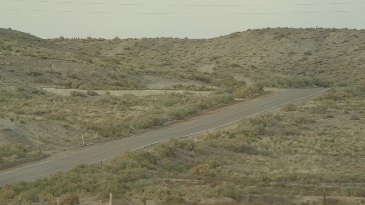 广角沙漠公路或乡村道路通过沙漠景观。长满灌木的干燥山坡。视频素材