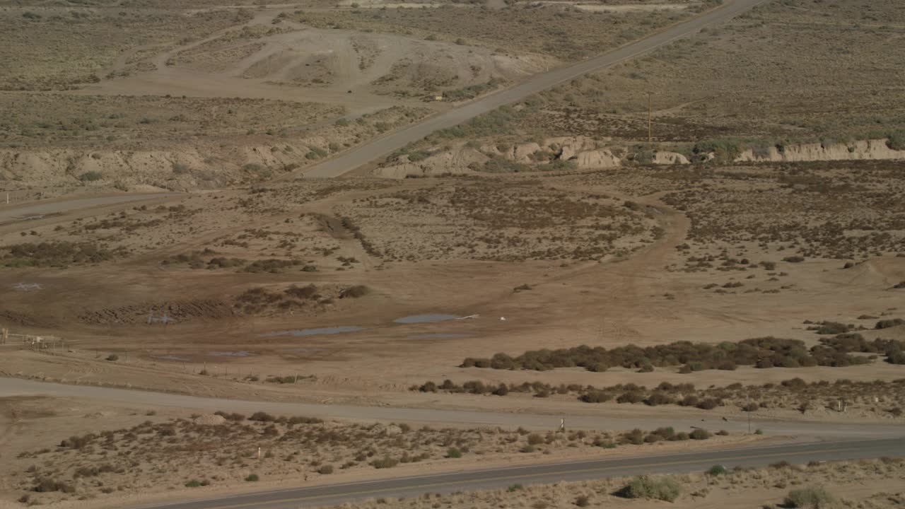 广角沙漠公路穿越平坦的沙漠地区。峡谷和灌木丛可见。视频素材