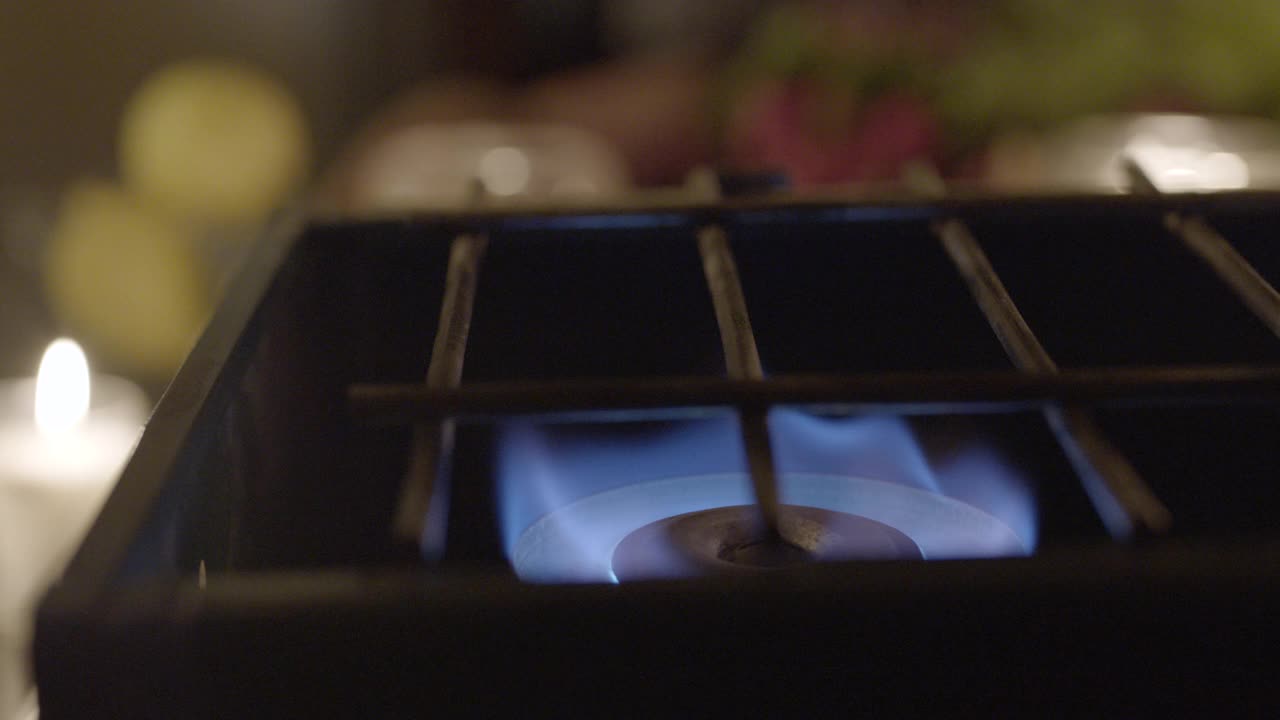 燃气燃烧器的闭合角度。火焰点燃并可见。可能是厨房。在bg中部分可见的蜡烛。视频素材