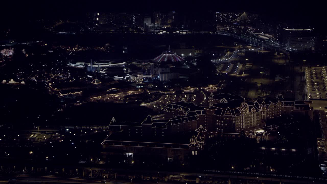 东京迪斯尼乐园酒店和东京迪斯尼乐园乐园的航拍。酒店的屋顶装饰被灯光照亮。太空山和itÕs一个小世界骑在bg可见。视频素材