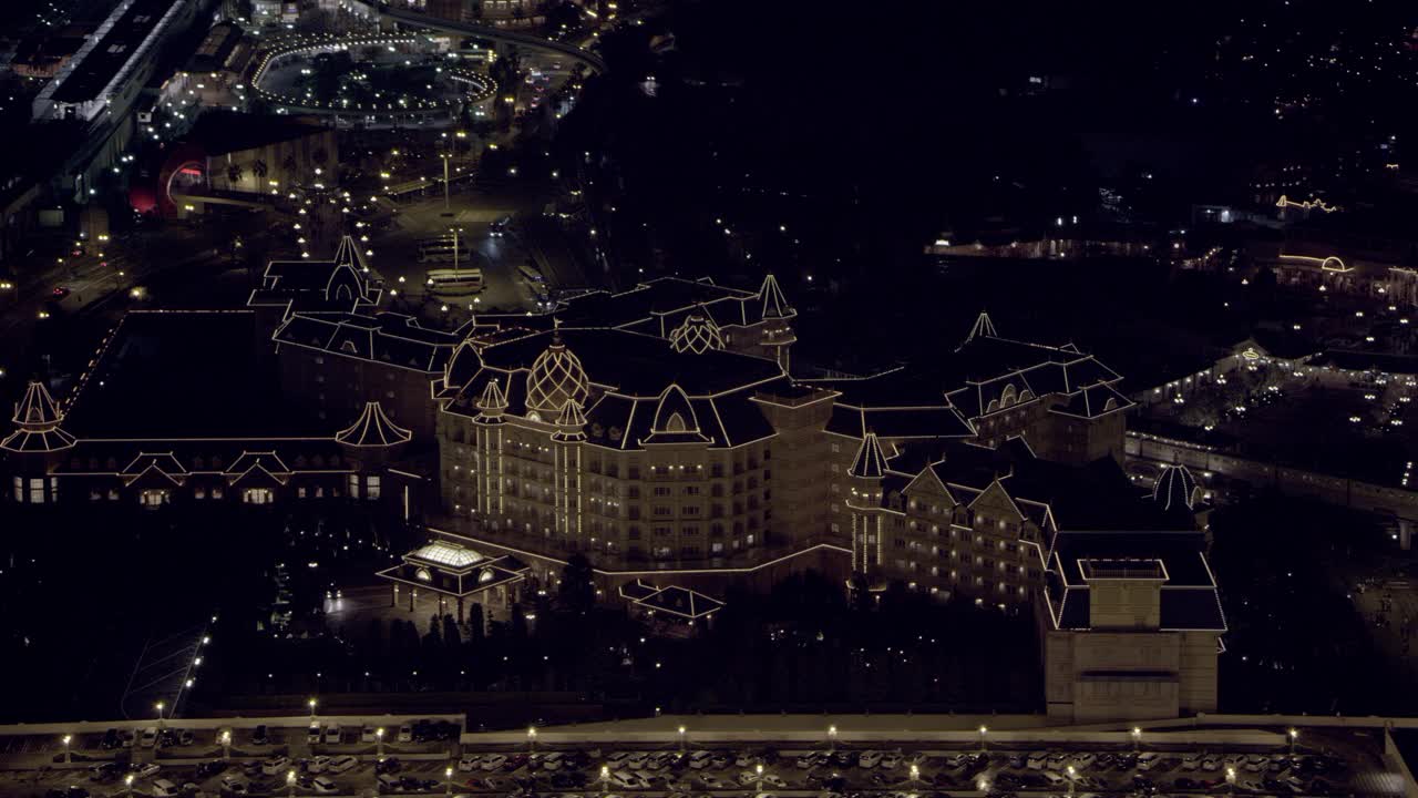 空中环视东京迪斯尼乐园酒店到东京迪斯尼乐园的广角。酒店的屋顶装饰被灯光照亮。太空山和itÕs一个小世界骑在bg可见。视频素材