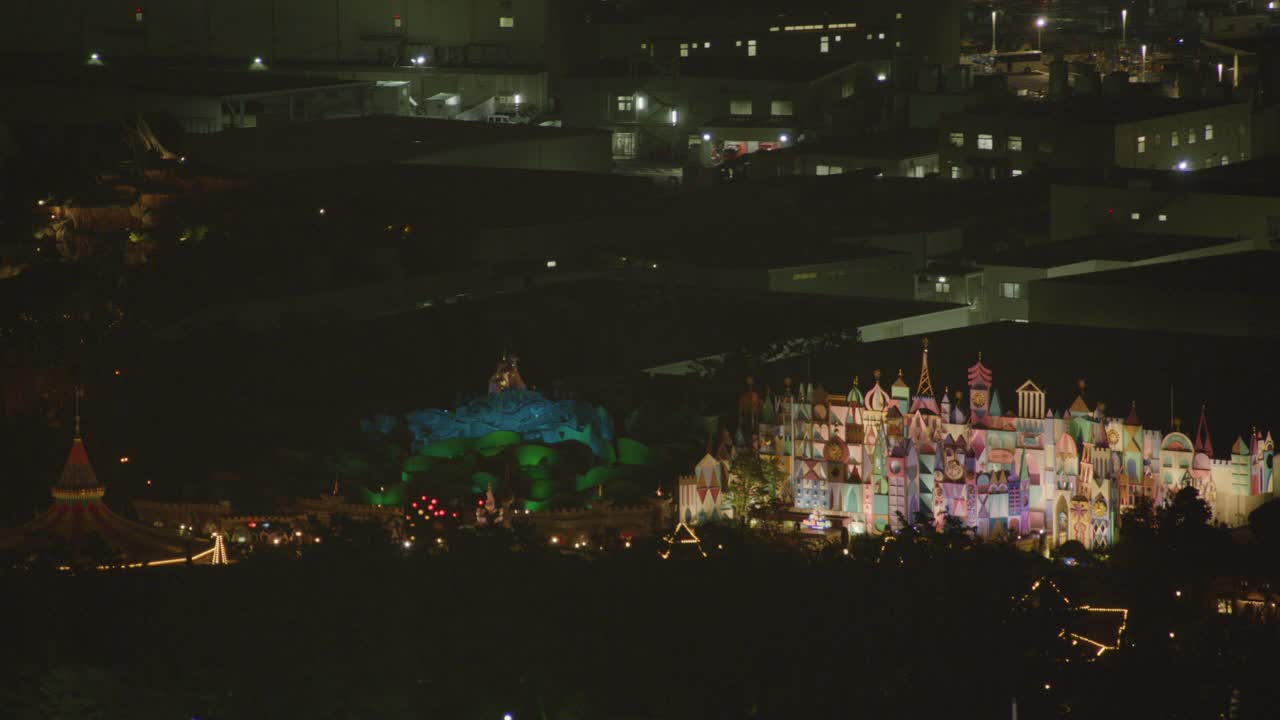 从itÕs的空中拉回来一个小世界骑到广角东京迪士尼乐园和东京迪士尼酒店。酒店的屋顶装饰被灯光照亮。可见太空登山之旅。视频下载