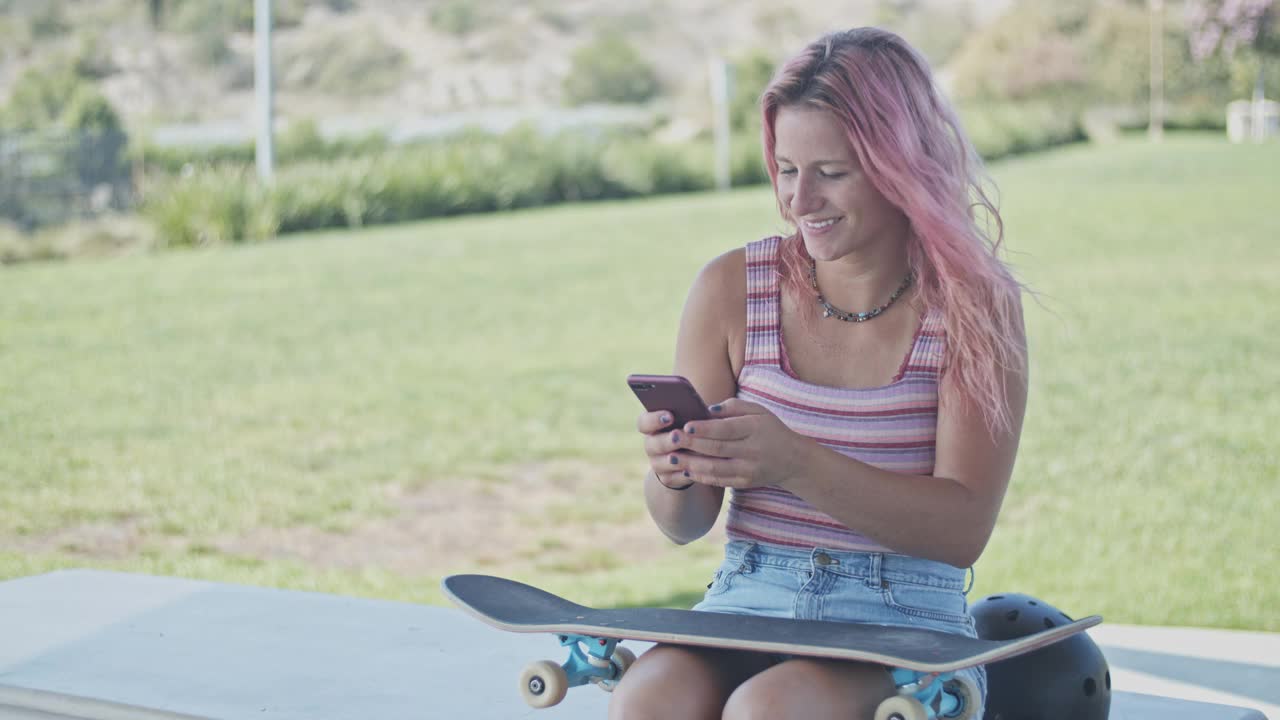 一个粉色头发的年轻女人在公园里用手机视频素材