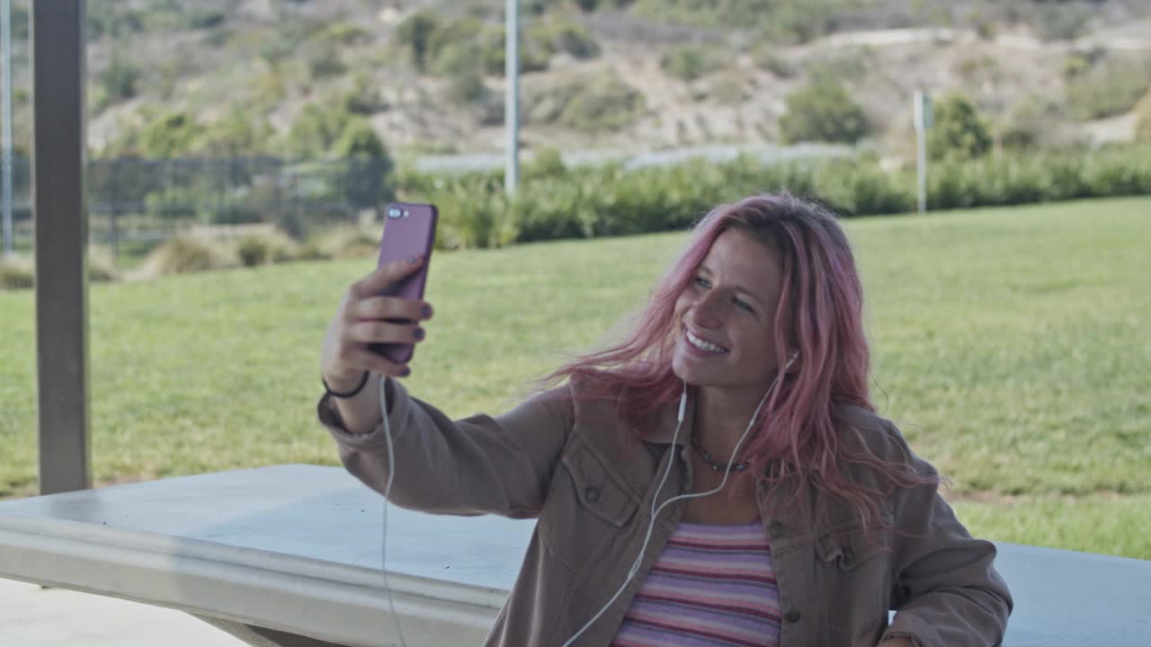 一个粉色头发的年轻女人在公园里用手机视频素材