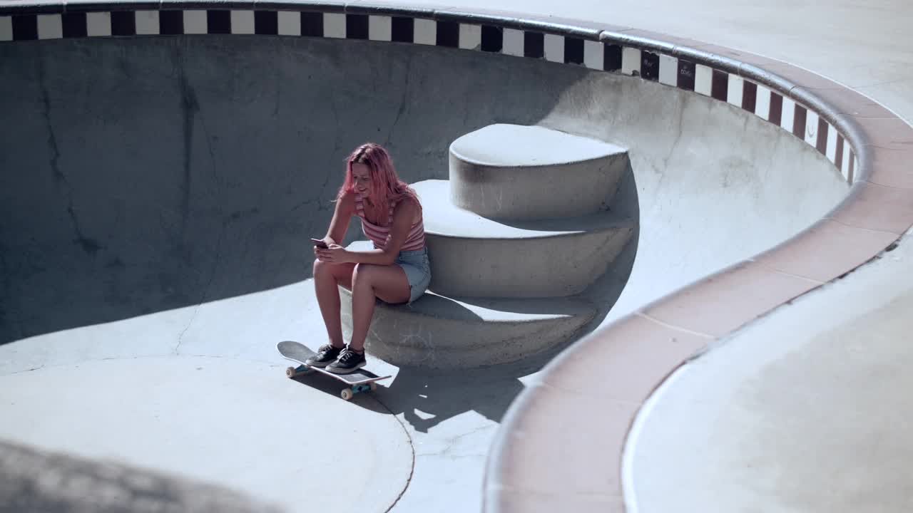 一个粉红色头发的年轻女子在滑板公园闲逛视频素材