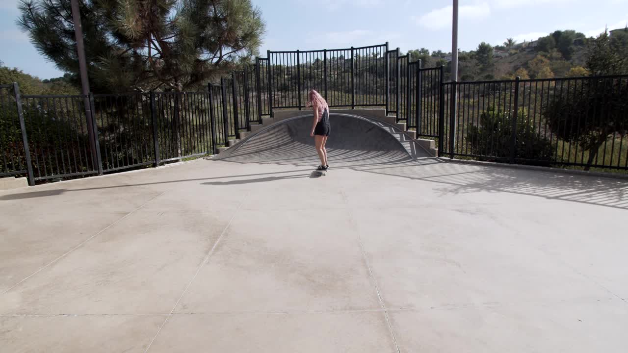一个粉红色头发的年轻女子在滑板公园溜冰视频下载