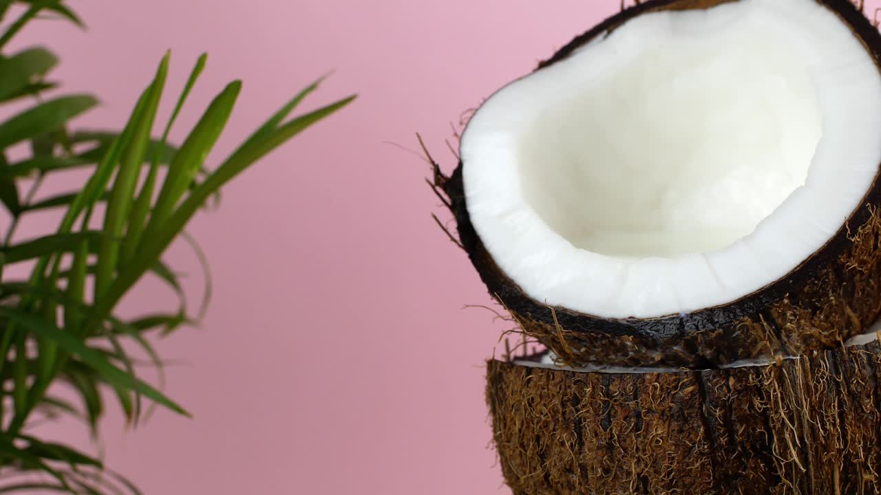 椰子螺母。多汁的成熟椰子被切开，椰子奶被倒在里面，粉红色的背景上有一棵绿色的棕榈树。视频素材
