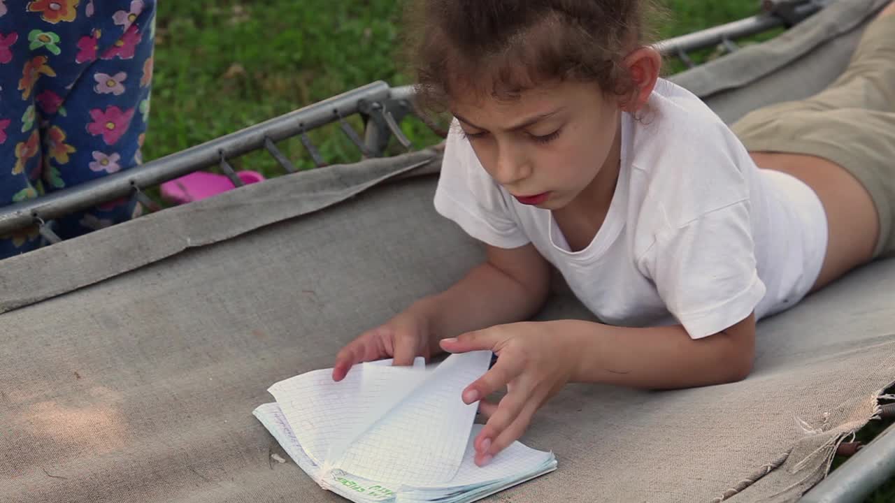 小女孩躺在后院的露营床上，大声读着笔记本上的笔记视频下载