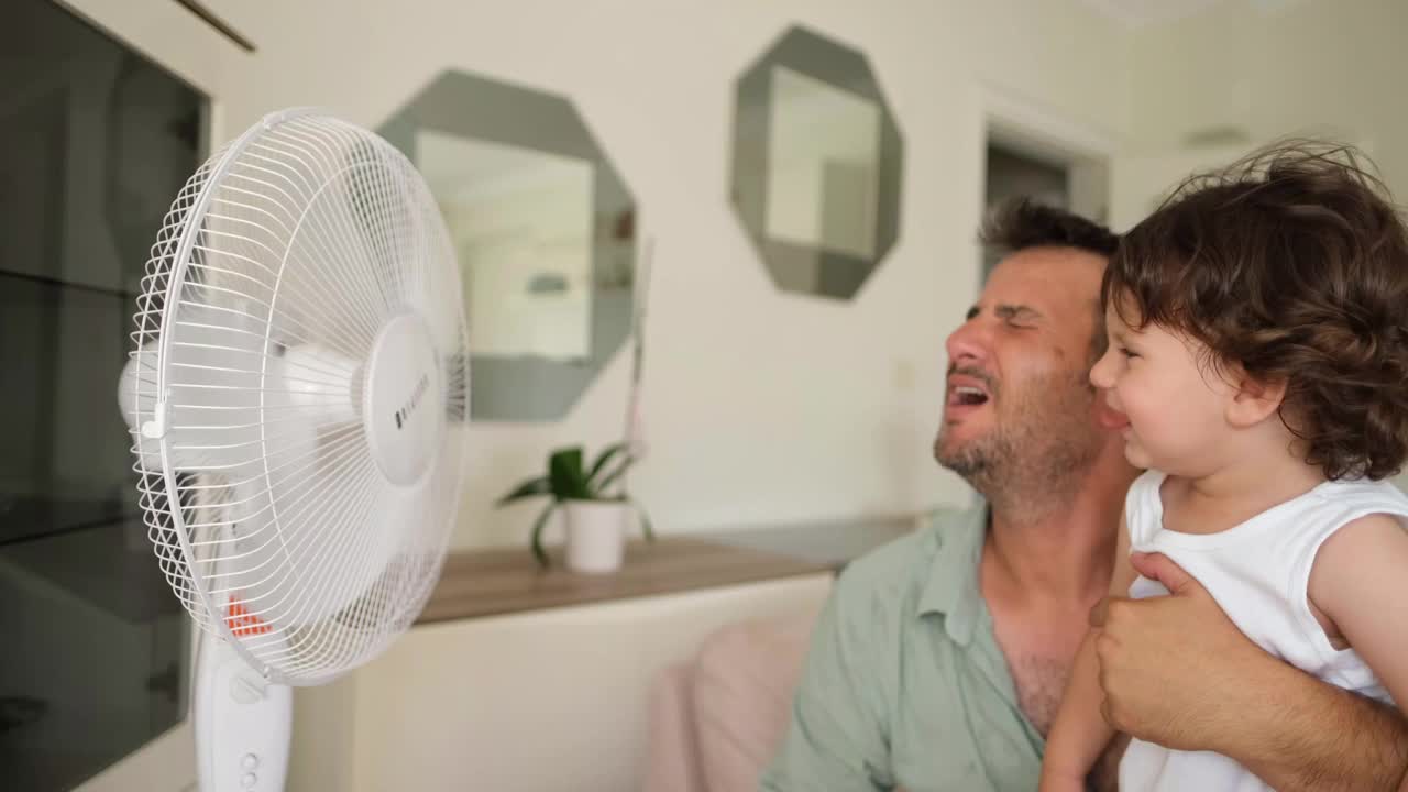 父亲孩子在炎热的夏天对着电风扇视频下载