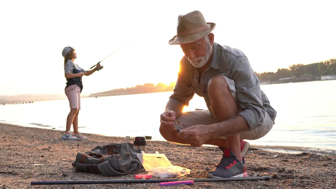 兴奋的爷爷正在准备下一次扫荡的鱼饵，而他的孙子在他身后，正在钓第一条鱼视频素材
