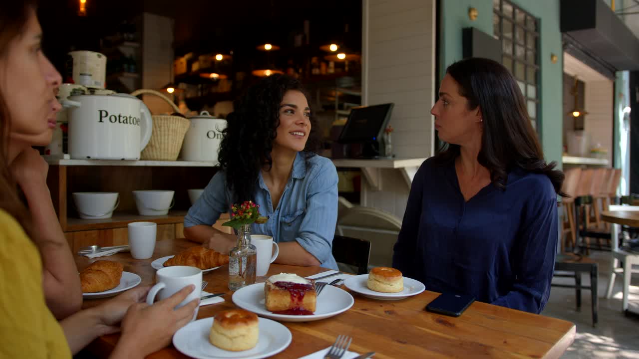 一个美丽的女人和她的朋友在咖啡馆度过了一天，一边聊天一边微笑着拍下他们的零食，准备发到社交媒体上视频素材