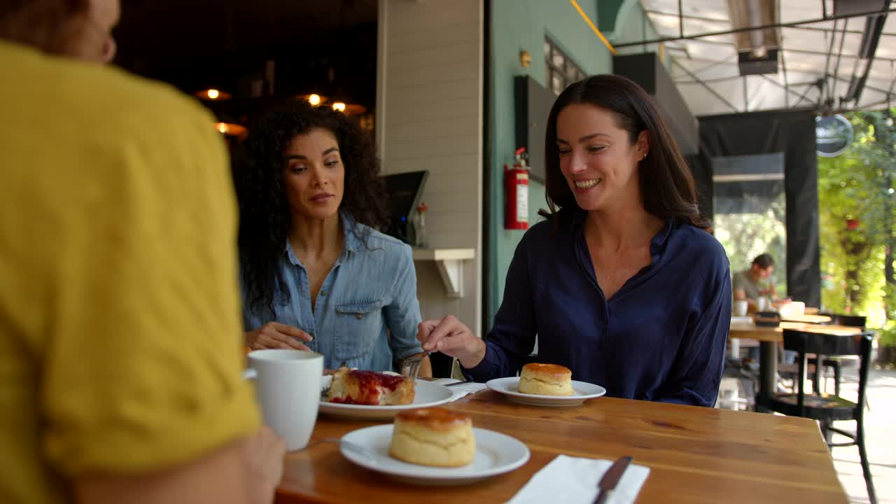 快乐的女性朋友在咖啡店边聊天边分享甜点视频素材