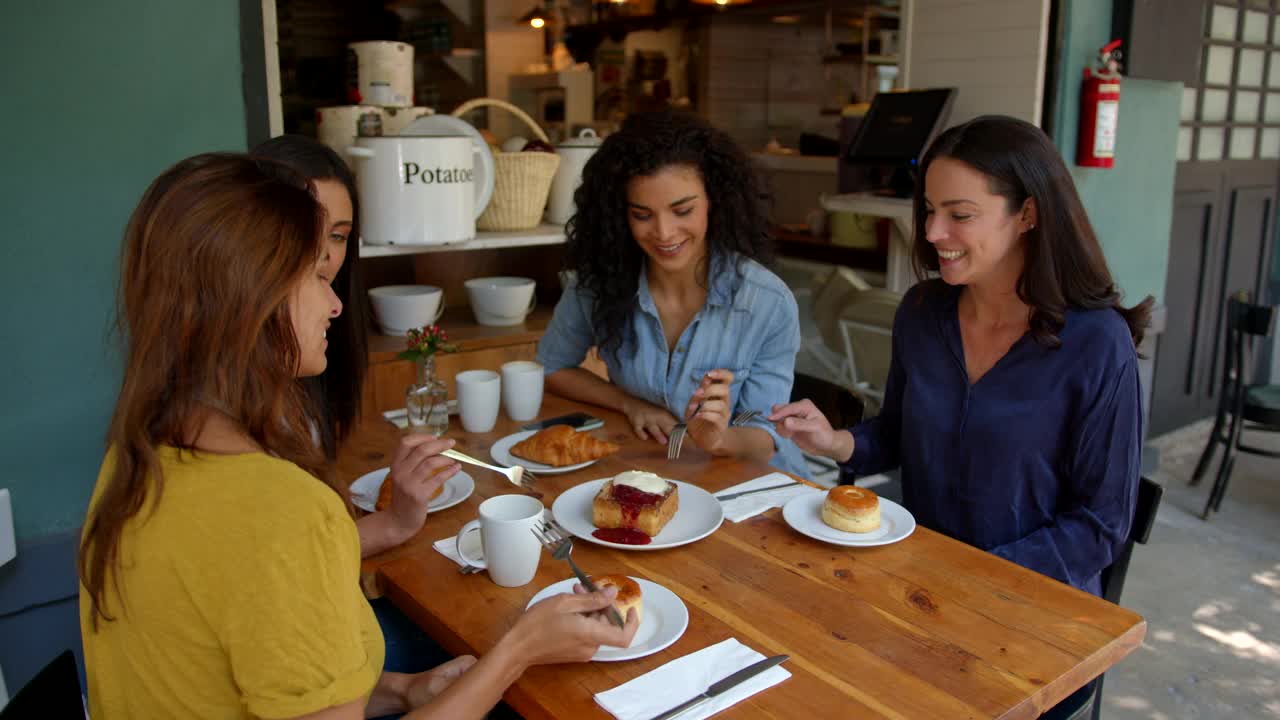 一群美丽的朋友在咖啡店边聊天边微笑，享受着甜点视频素材