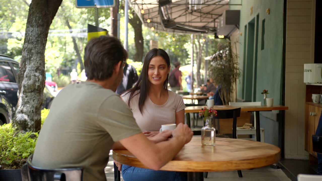 一个快乐的女人在约会时，坐在咖啡馆的露天桌子前进行非接触式支付，而服务员拿着信用卡读卡器视频下载
