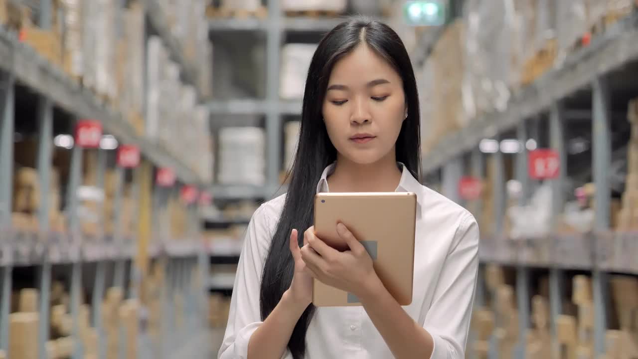 迷人的亚洲年轻女工仓库工人手握平板电脑和清单在仓库。仓库的概念视频下载