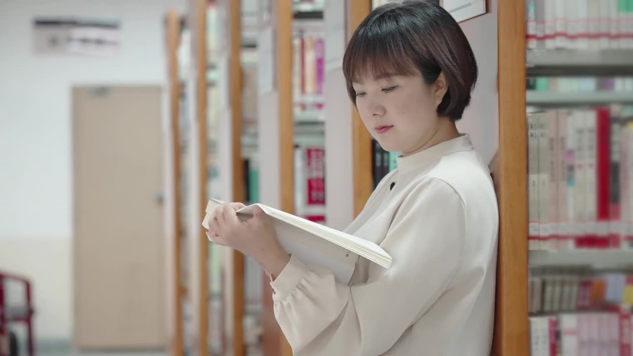 亚洲女人在图书馆的书架上看书视频素材