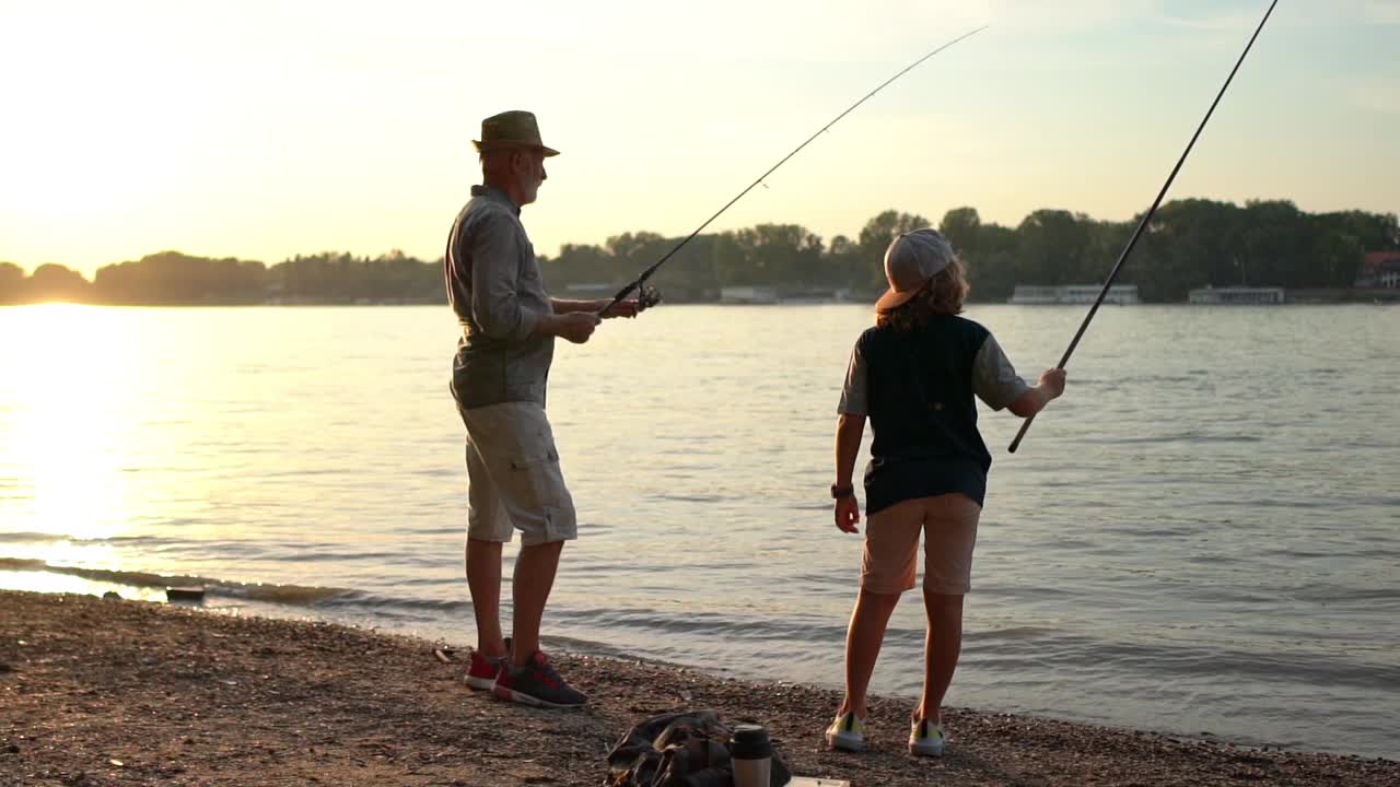 老渔夫，和他的孙子一起欣赏河上的日落，两人都在钓鱼中度过了一天的最后视频素材