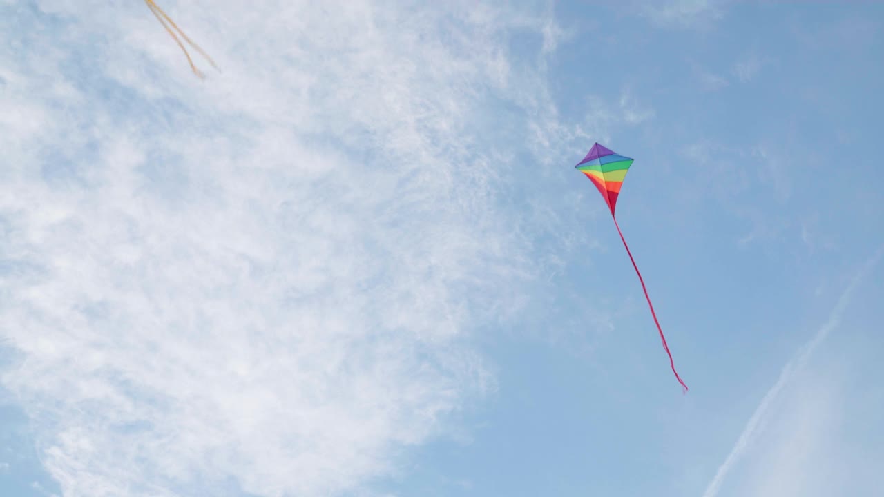 4K五颜六色的风筝在蔚蓝的天空中飞翔，一阵风吹来，白云高高飘起视频素材