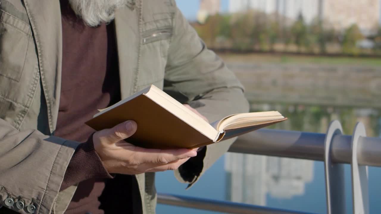 白种人男子手持书的特写镜头。一个不知名的退休老人在阳光明媚的户外读书视频素材