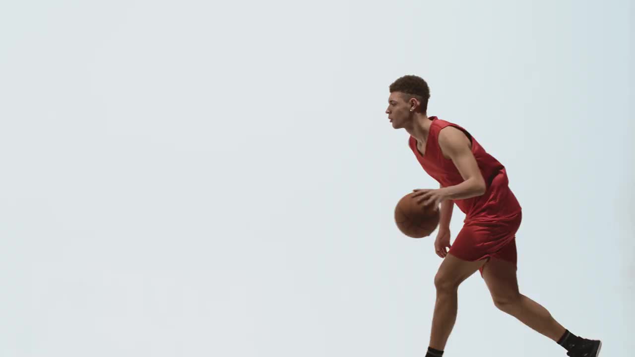 侧视图或年轻的篮球运动员在红色运动服运行和运球在白色工作室背景。运动员正在训练中为比赛做准备。慢动作准备59.94帧视频下载