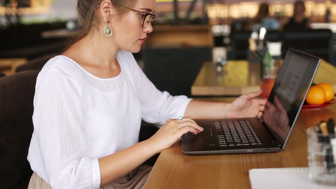 混合种族自由职业者转换笔记本电脑到平板电脑，而工作在咖啡馆。亚洲白人女商人与变压器笔记本。数码艺术家使用触摸屏二合一电脑视频素材