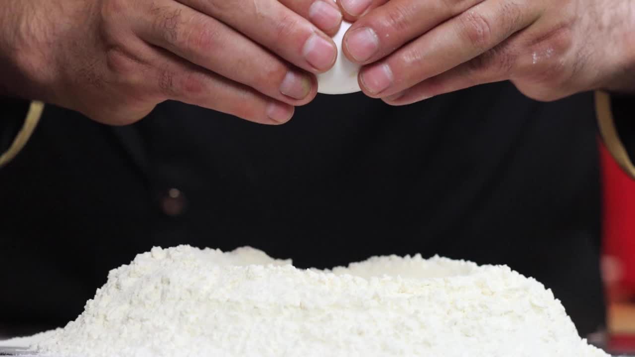 生鸡蛋落在一堆面粉上，背景为黑色，慢镜头拍摄。视频素材