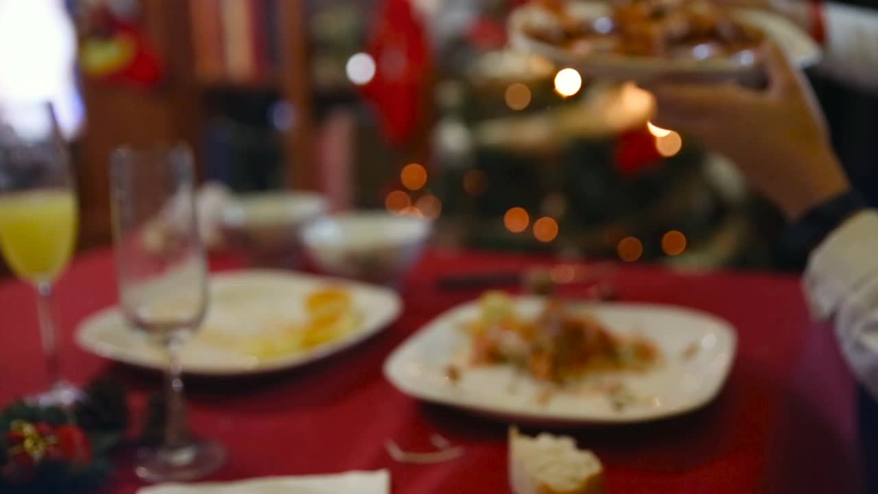 一只手伸到一盘大虾上，放在家庭的圣诞餐桌上，身后是圣诞树上的彩灯视频素材