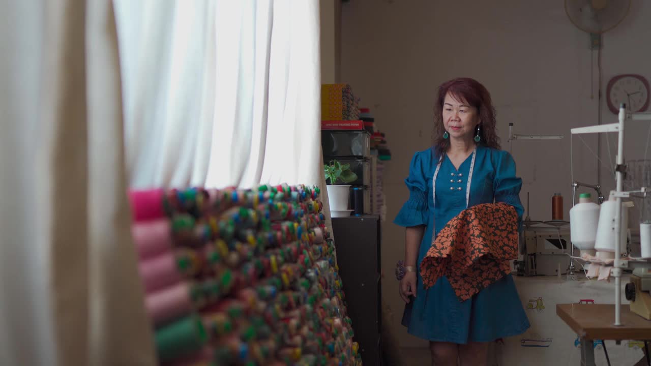 亚洲华人高级女性裁缝在工作室工作室选择丝线搭配面料服装视频素材