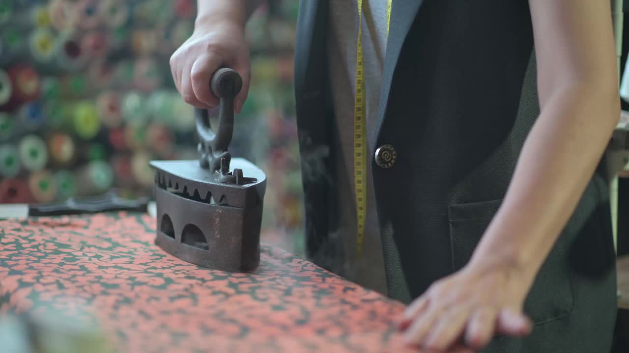 近距离拍摄亚洲华人高级妇女裁缝手用传统古玩铁器具在她的工作室熨布视频素材