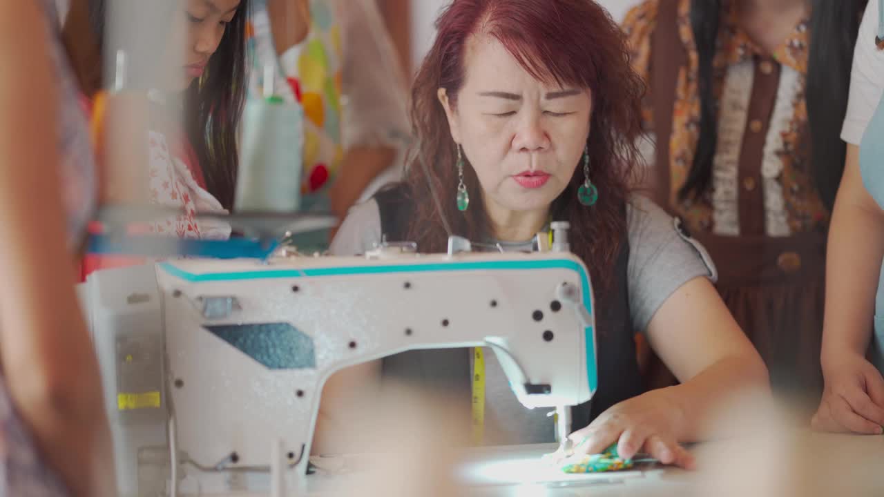 亚洲华人高级妇女裁缝教学展示她的学生在缝纫课在工作室工作坊视频下载