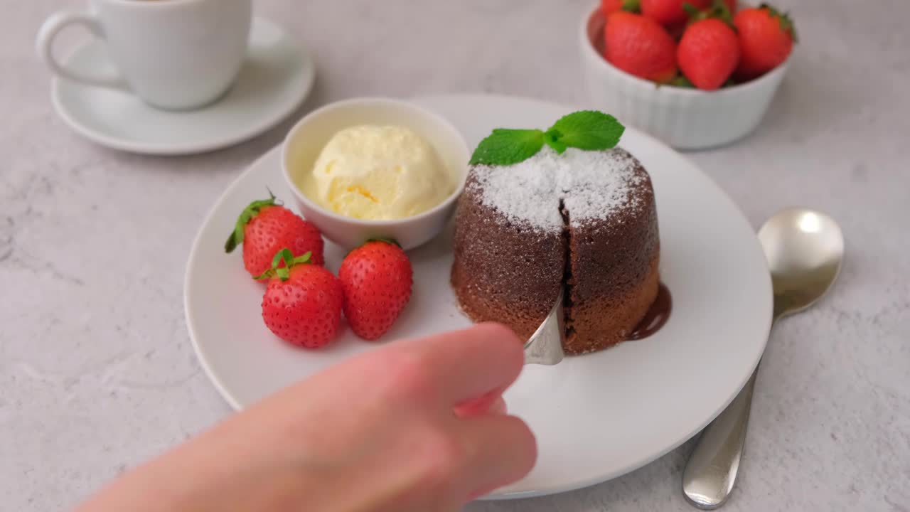 熔岩蛋糕是一种巧克力蛋糕，里面有香草冰淇淋、草莓、薄荷和咖啡。传统的法国糕点。女人的削减视频素材