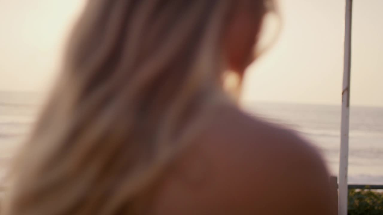 年轻的金发女人在日落时看海的肖像视频下载