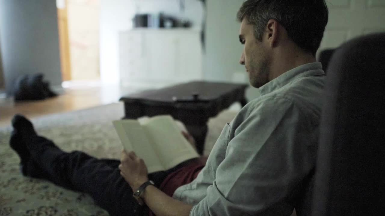 一名男子一边看书一边用手机应用控制家里的灯视频素材