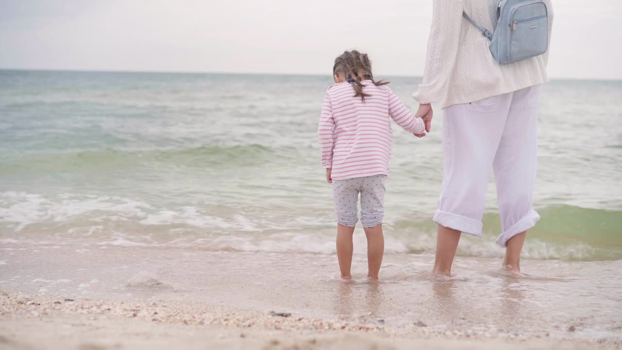 妈妈带着小女儿在海边散步海滩上快乐的一家人妈妈牵着小孩子在海边散步。暑假旅行视频素材