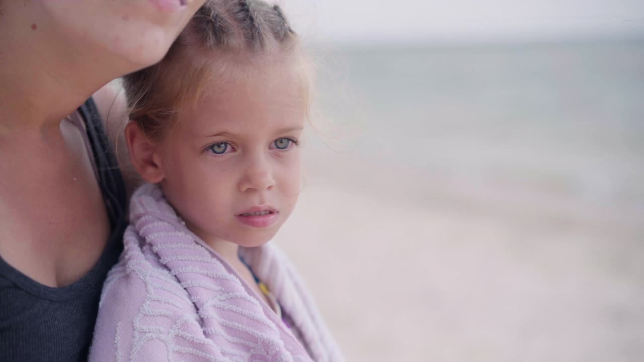 妈妈拥抱着温暖着小女儿把毛巾擦在户外阳光灿烂的沙滩上视频素材