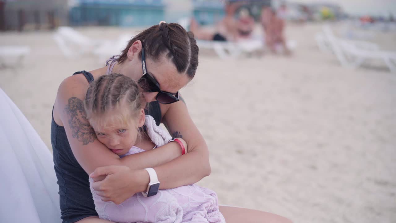 妈妈拥抱着温暖着小女儿把毛巾擦在户外阳光灿烂的沙滩上视频素材