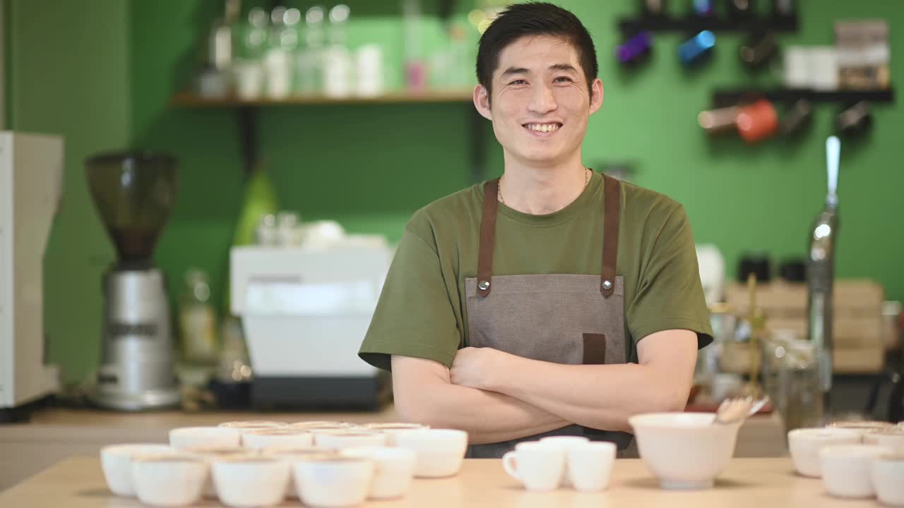 一位亚洲华裔咖啡师在咖啡厅柜台前双臂交叉，望着镜头微笑视频素材