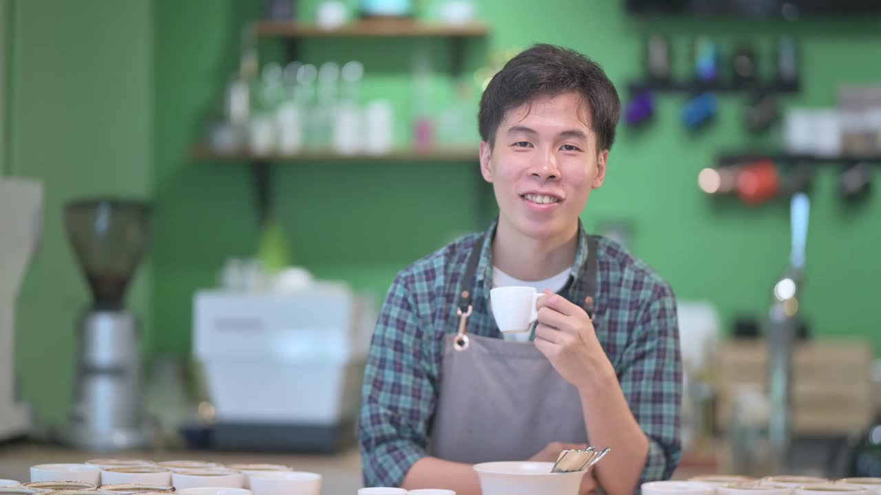 肖像华人咖啡师在咖啡厅柜台边微笑着拿着咖啡杯视频素材