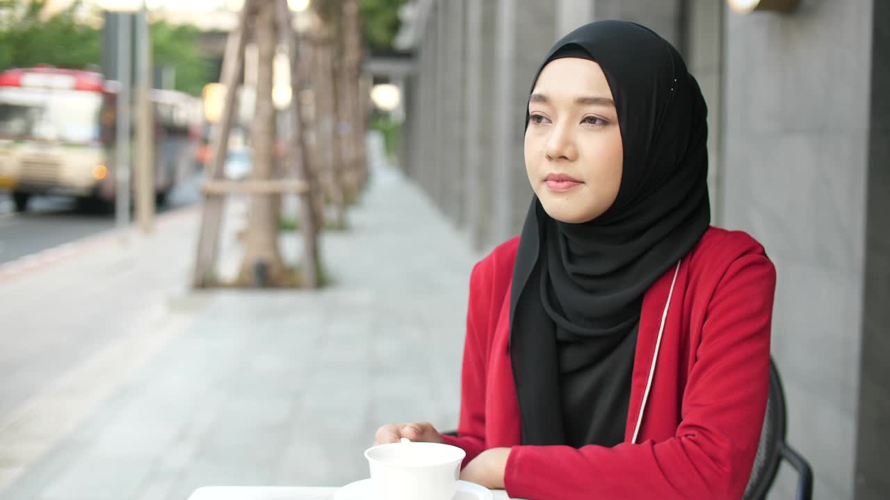 美丽的穆斯林妇女戴着头巾，在户外喝着咖啡，微笑着看着相机视频下载