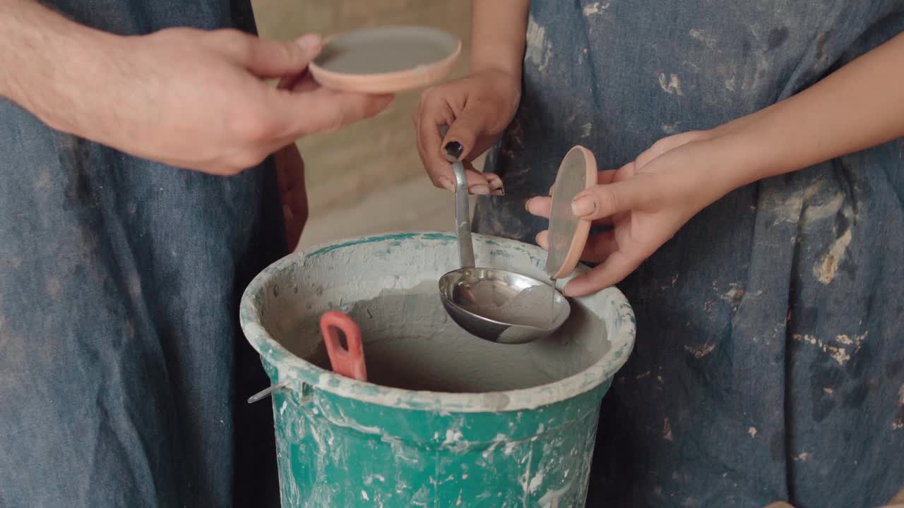 两个陶工在他们的陶器车间工作时，将粘土添加到他们的手工盘子中。视频下载