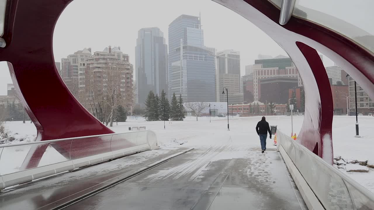 步行交通走过一个巨大的红色人行天桥走向一个有雪的城市。视频素材
