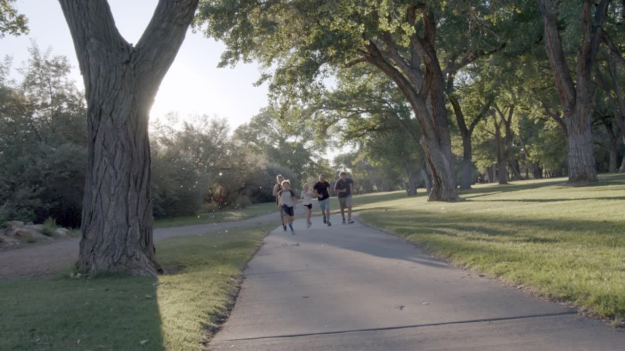 年轻的家庭，父亲母亲两个男孩和一个年幼的女儿在黄昏时一起在公园里奔跑视频素材